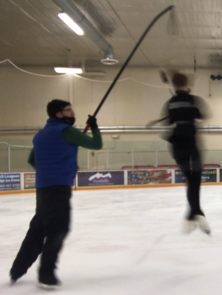 Coach Nick supporting a skater’s jump with a pole harness